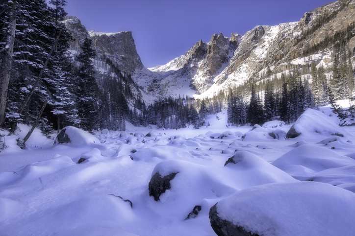Snow drifts form over the boulders along the frozen shoreline of Dream lake, a popular high altitude lake located in Rocky Mountain National Park