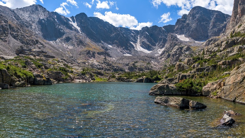A panoramic view of clear and colorful Lake of Glass surrounded by rugged high peaks of Continental Divide on a sunny Summer day.